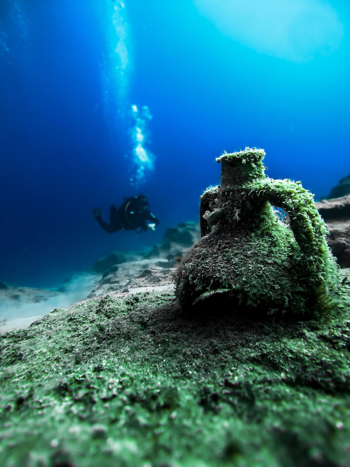 An ancient amphora on the bottom with a diver behind in Kaş